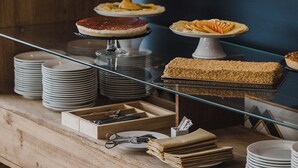 A buffet setup with various dishes on stands, plates stacked on the counter, and a wooden table with utensils and napkins.