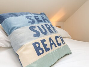 A bed with a pillow featuring the text "SEA SURF BEACH". - Honeysuckle Cottage (Barnstaple)