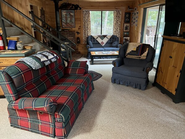 A cozy living room with a plaid sofa, a blue armchair, and a wooden staircase.