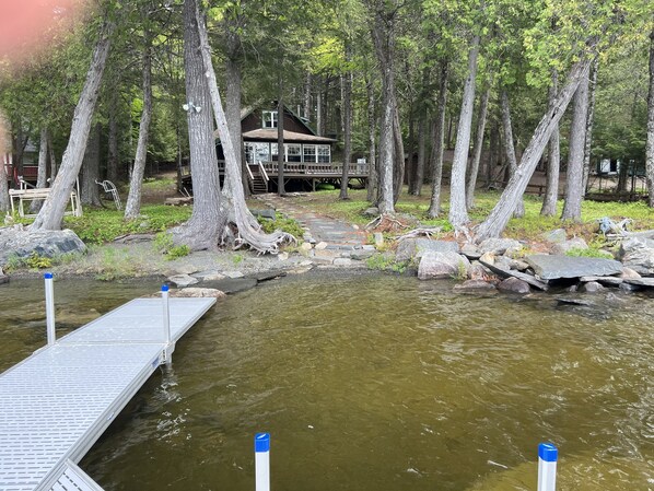 Une cabane entourée de grands arbres, une jetée s’avançant dans une rivière paisible et une terrasse en bois dotée de rampes.