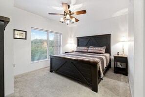 A bedroom with a dark wooden bed, a ceiling fan, two bedside lamps, a window with blinds, and a framed picture on the wall.