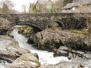 Eine Steinsbrücke über einem Fluss mit steinernen Ufern und einem Gebäude im Hintergrund.