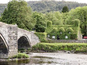 Eine Steinbrücke über einem Fluss, im Hintergrund ein mit Efeu bewachsenes Haus.