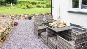 An outdoor patio with wicker furniture, a table with food and drinks, and a stone wall. - Coed Derw Isaf (Betws-Y-Coed)