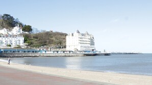 A coastal hotel with a prominent white building, a pier extending into the water, and a sandy beach area. - Coed Derw Isaf (Betws-Y-Coed)