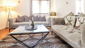 A living room with a sofa, a coffee table, a lamp, and a patterned rug. - Coed Derw Isaf (Betws-Y-Coed)