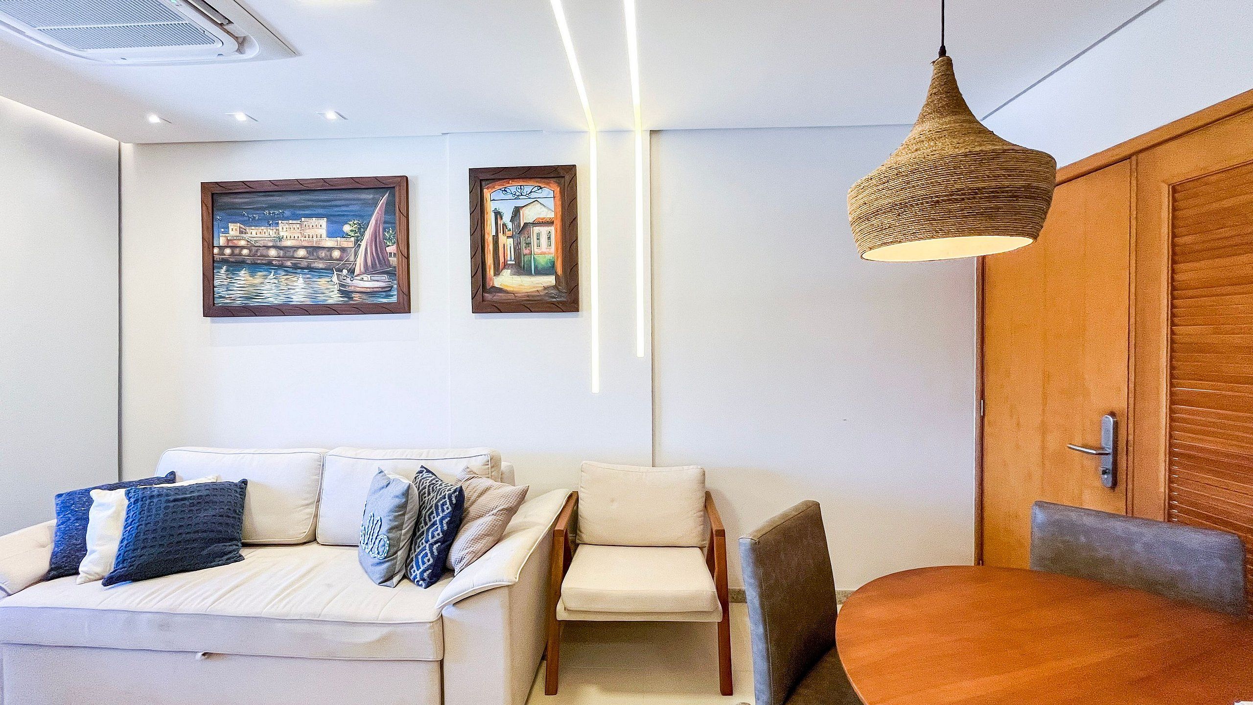 A modern living room with a sofa, a dining table, and two framed paintings on the wall.