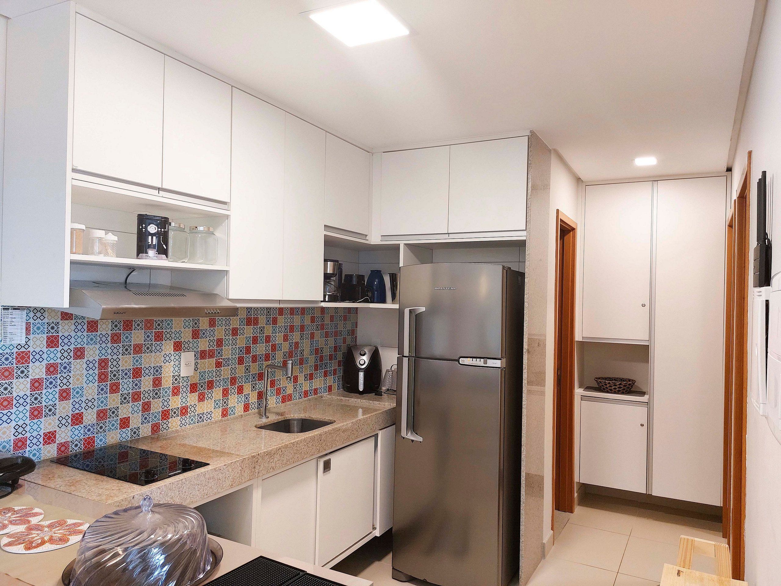 A compact kitchen with white cabinets, a stainless steel refrigerator, a tiled backsplash, and a coffee maker.