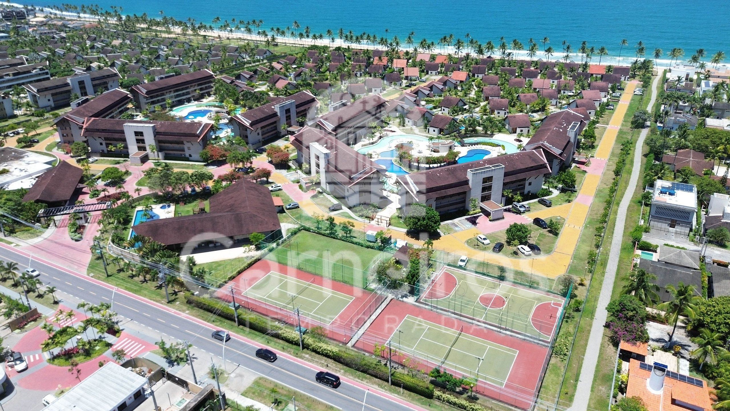Vista aérea de um resort com vários edifícios, uma piscina e quadra de tênis.