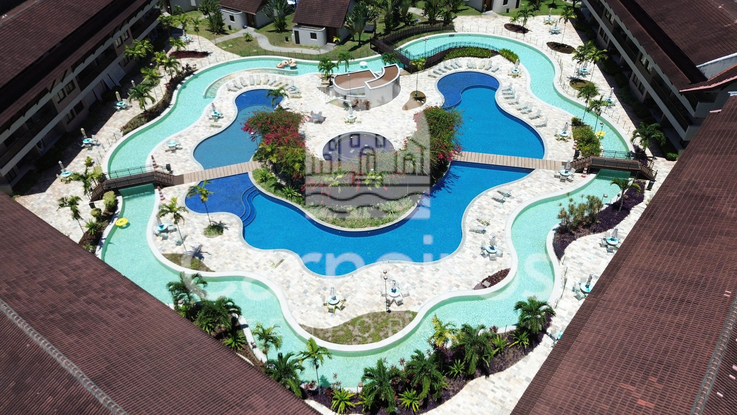 A large, multi-pool resort with a central circular pool surrounded by smaller pools and sunbathing areas.