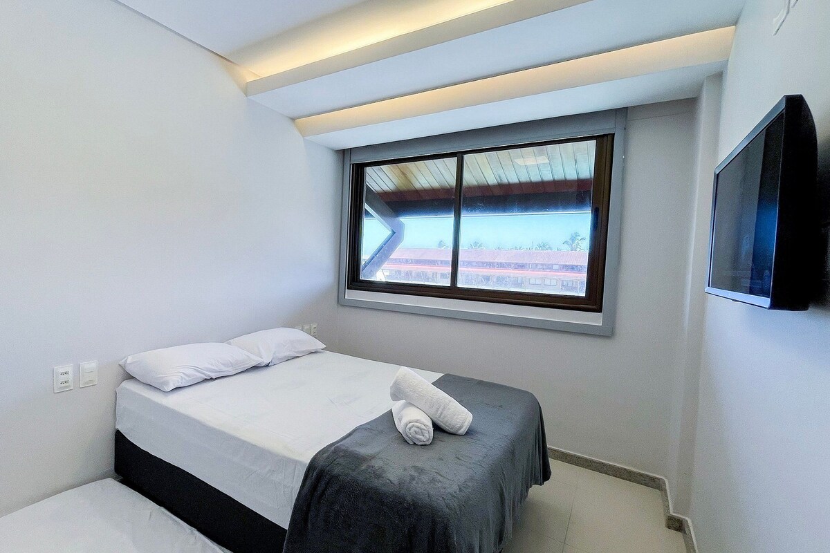 A bedroom with a bed, a window with a view, a flat-screen TV, and a ceiling light.