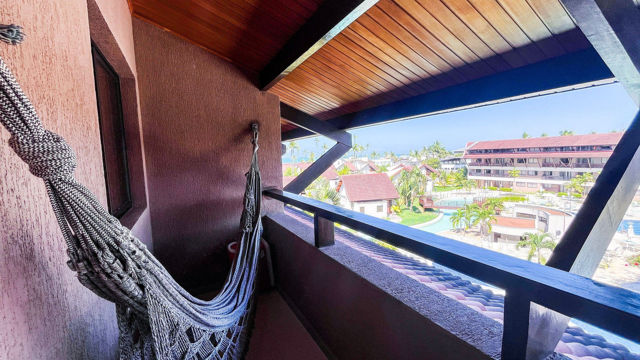 Una hamaca colgada del barandal de un balcón, con vistas a una zona residencial con casas y cielo despejado.