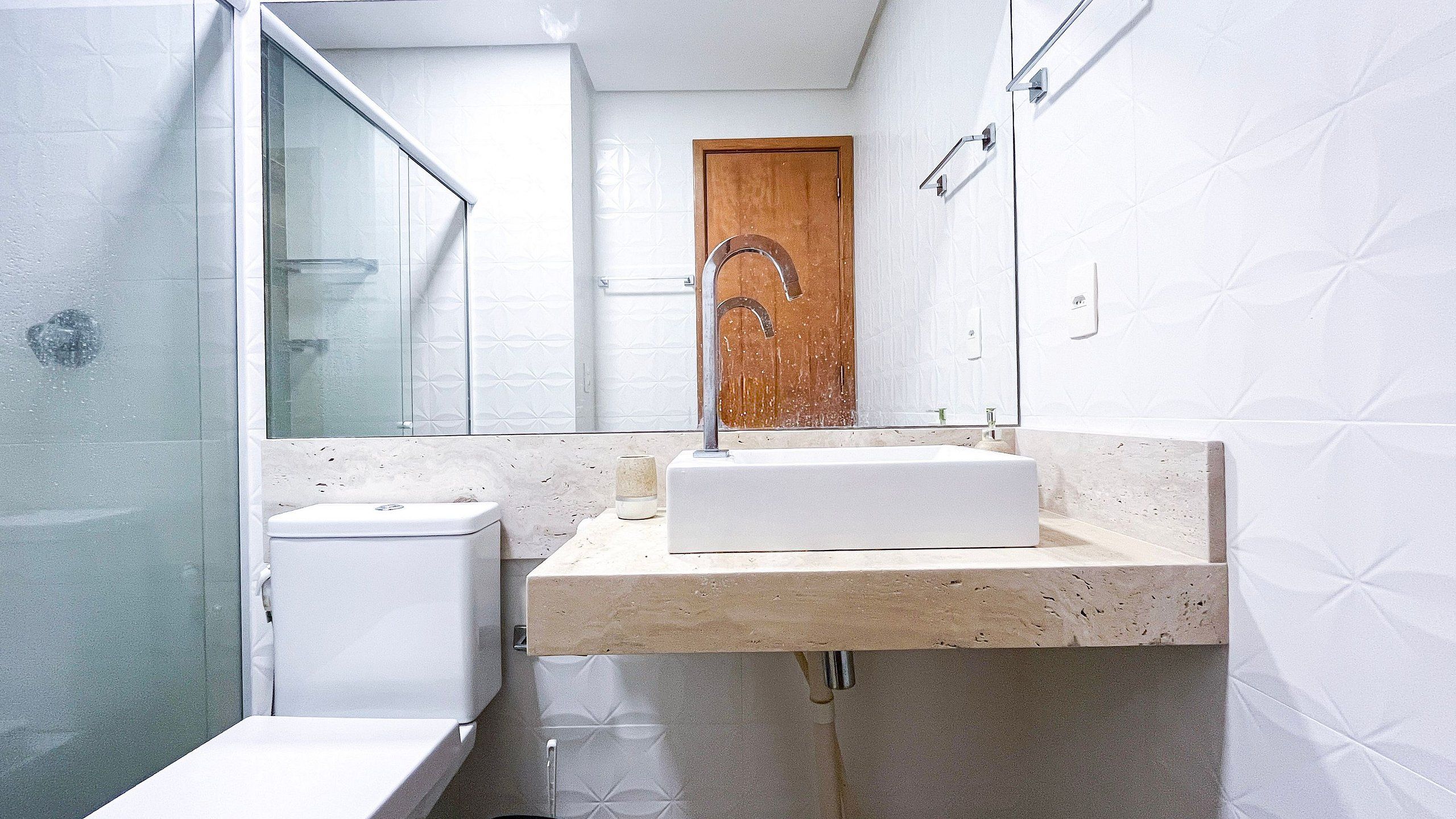 Ein Badezimmer mit Duschkabine aus Glas, Toilette, Waschbecken mit Spiegel und Holztür.