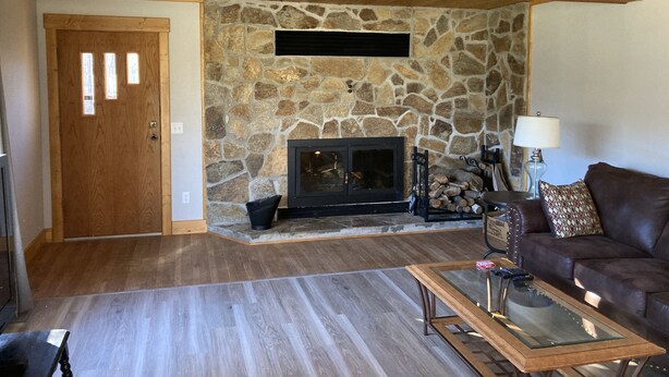 Una sala de estar acogedora con chimenea de piedra, techo de madera y un sofá de cuero marrón.