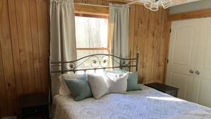 Un dormitorio con paneles de madera, una cama, almohadas, una mesita de noche y una puerta.