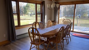 Un comedor con mesa y sillas de madera, ventanas amplias y vista a un patio.