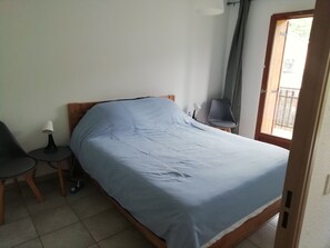 A room with a bed, a chair, a small table with a lamp, and a window with a curtain. - Guillestre, 2-room apartment with a terrace, near the shuttle buses to the ski resorts in Queyras (Guillestre)
