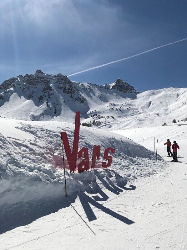 A snowy mountain landscape with a large red sign reading "Vans" and skiers on the slope. - Guillestre, 2-room apartment with a terrace, near the shuttle buses to the ski resorts in Queyras (Guillestre)