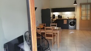 A modern kitchen with a built-in washing machine, a dining area with wooden chairs, and a TV on a stand. - Guillestre T2 with terrace, close to shuttles to Queyras resorts (Guillestre)