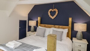 A bedroom with a wooden headboard, a heart-shaped wall decoration, two bedside tables with lamps, and a bed with a checkered bedspread and folded towels. - Old Town House (Dawlish)