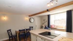 A modern kitchen with wooden flooring, a central island with a stove, and a dining area with chairs and a table. - Old Town House (Dawlish)