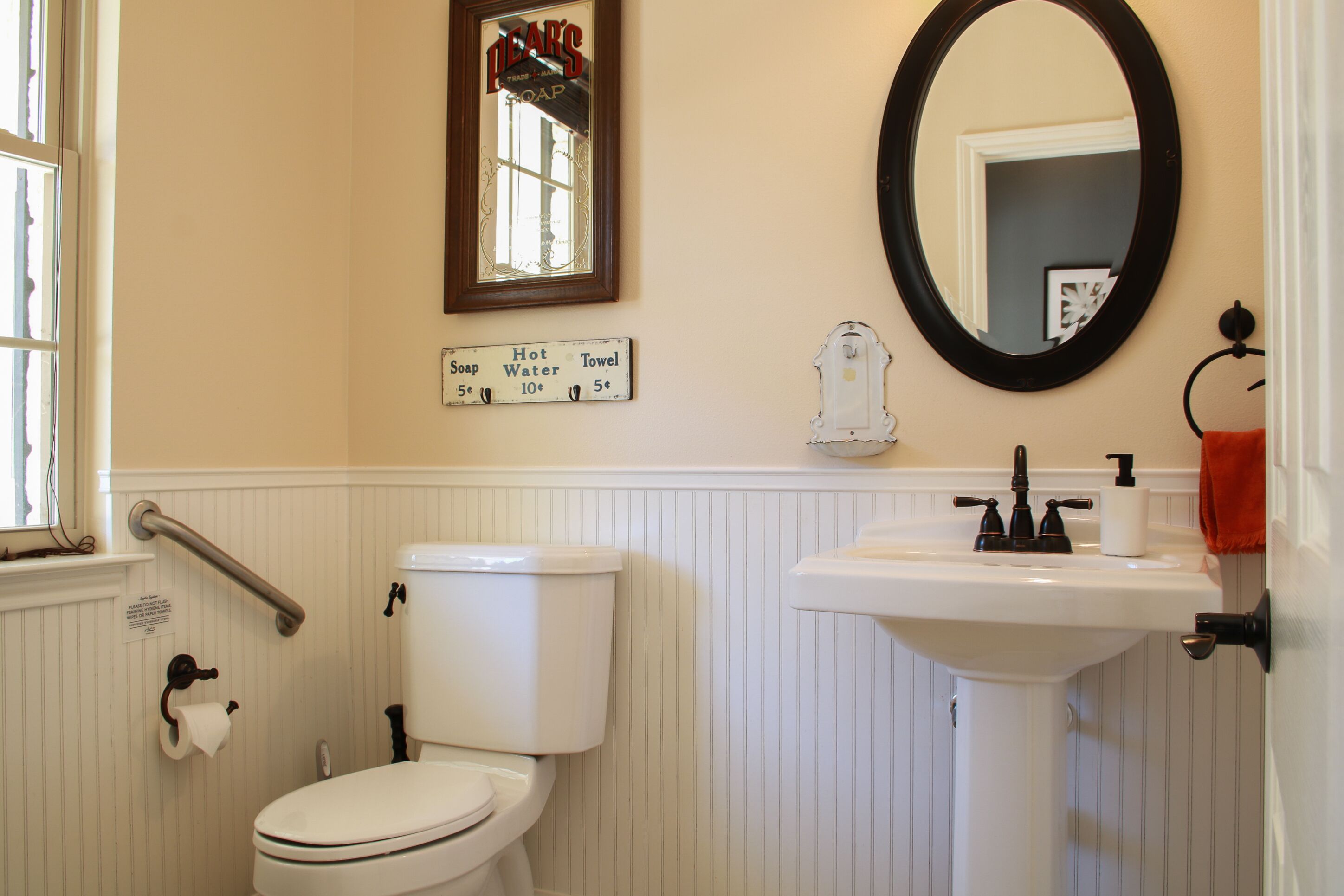 Une salle de bain avec des toilettes, un lavabo et un miroir. Au-dessus du lavabo, une affiche indique les prix du savon, de l’eau chaude et des serviettes.