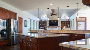 Una cocina amplia con una isla grande, electrodomésticos de acero inoxidable, armarios de madera y una chimenea de piedra.