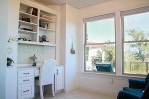 Ein Zimmer mit Schreibtisch, Regalen mit Büchern, einem Stuhl und einem Fenster mit Blick ins Freie.