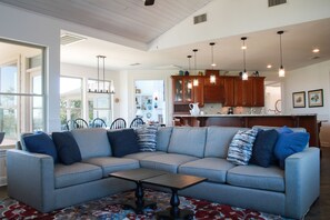 Ein großzügiges Wohnzimmer mit einer grauen Eckcouch, einem Couchtisch und einem gemusterten Teppich.