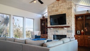 Un salón amplio con chimenea de piedra, un televisor de pantalla plana grande montado en la pared y una estantería empotrada.
