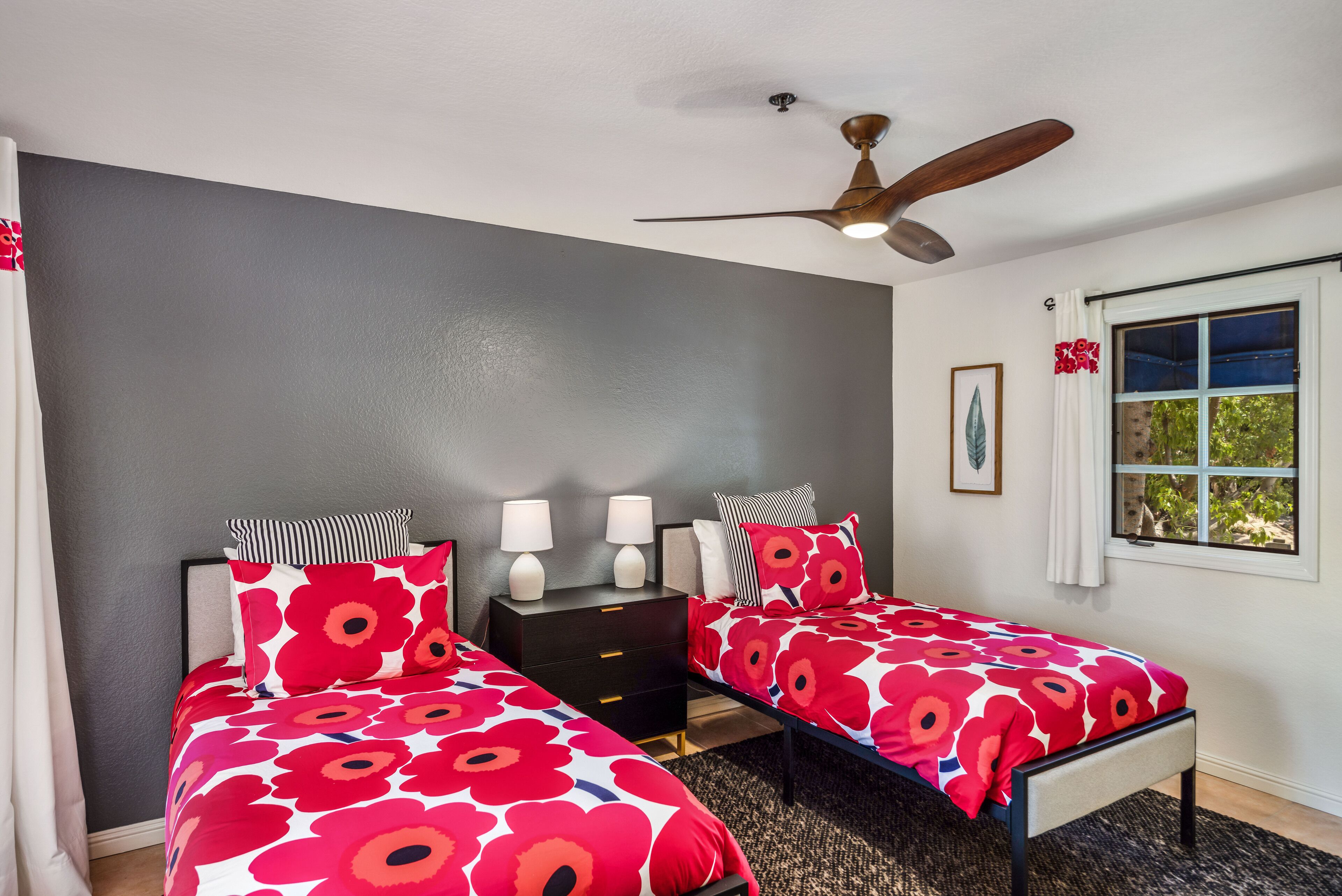 A bedroom with two beds, a ceiling fan, a nightstand, and a window with curtains.