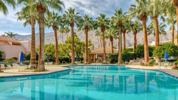 Une piscine entourée de palmiers, avec une chaîne de montagnes en arrière-plan.