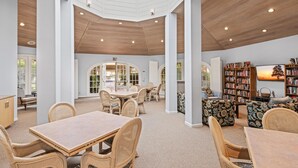 Un vaste espace intérieur doté d’un haut plafond, de poutres en bois et d’une lucarne. On y trouve plusieurs coins salon avec des meubles en osier et une grande bibliothèque remplie de livres.