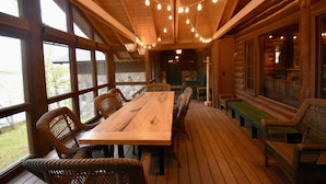 Eine Holzdielen-Terrasse mit Tisch, Stühlen, Lichterketten und großen Fenstern.