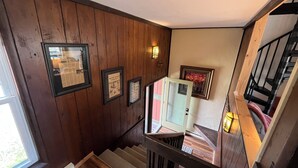 Eine Holztreppe mit Handlauf, ein gerahmter Zeitungsartikel und eine Wandleuchte.