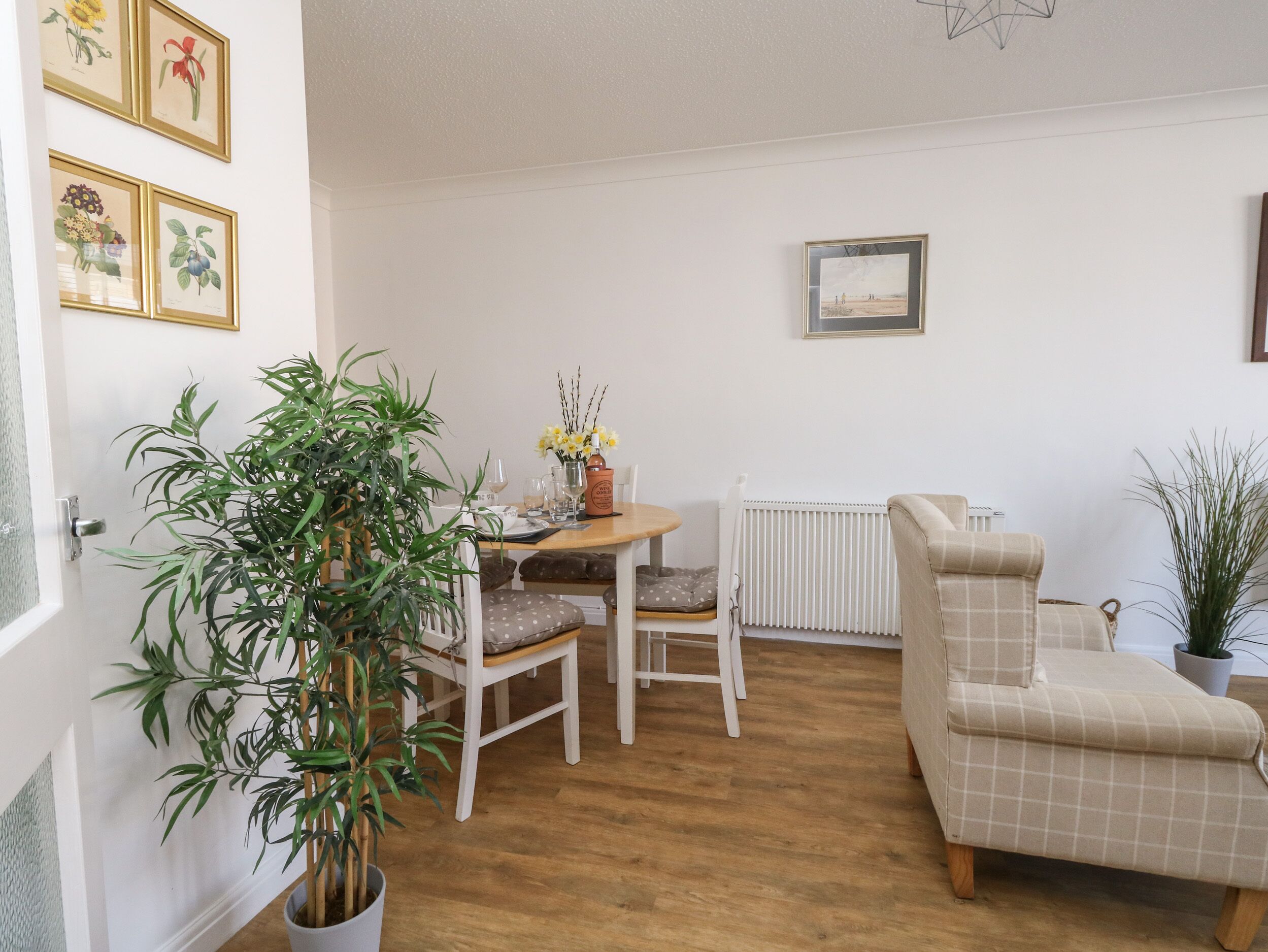 A cozy living room with a wooden floor, a dining table with chairs, a sofa, and a radiator.