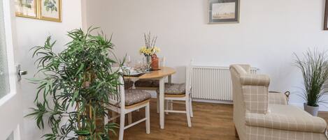 A cozy living room with a wooden floor, a dining table with chairs, a sofa, and a radiator.