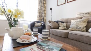 Una sala de estar acogedora con una mesa de centro de madera, un hervidor blanco, un plato con un pastel y un libro titulado 'West Bay'.