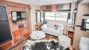 Een compact interieur van een camper met een kitchenette, een televisie, een bank en een kussen van ruitjesleer.