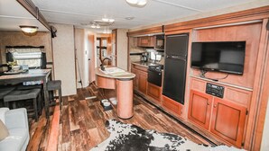 Een compacte camperkeuken met een spoelbak, kookplaat, koelkast en een flatscreen televisie aan de muur.