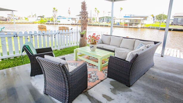 Een terras buiten met wicker meubels, een bijzettafeltje en uitzicht op een jachthaven.
