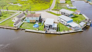 Luchtbeeld van een perceel aan het water met een steiger, een zwembad en meerdere gebouwen.