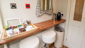 Bagno d'albergo con un mobile vanitario in legno, un lavandino bianco, una macchina per il caffè e un vassoio con articoli da toilette.