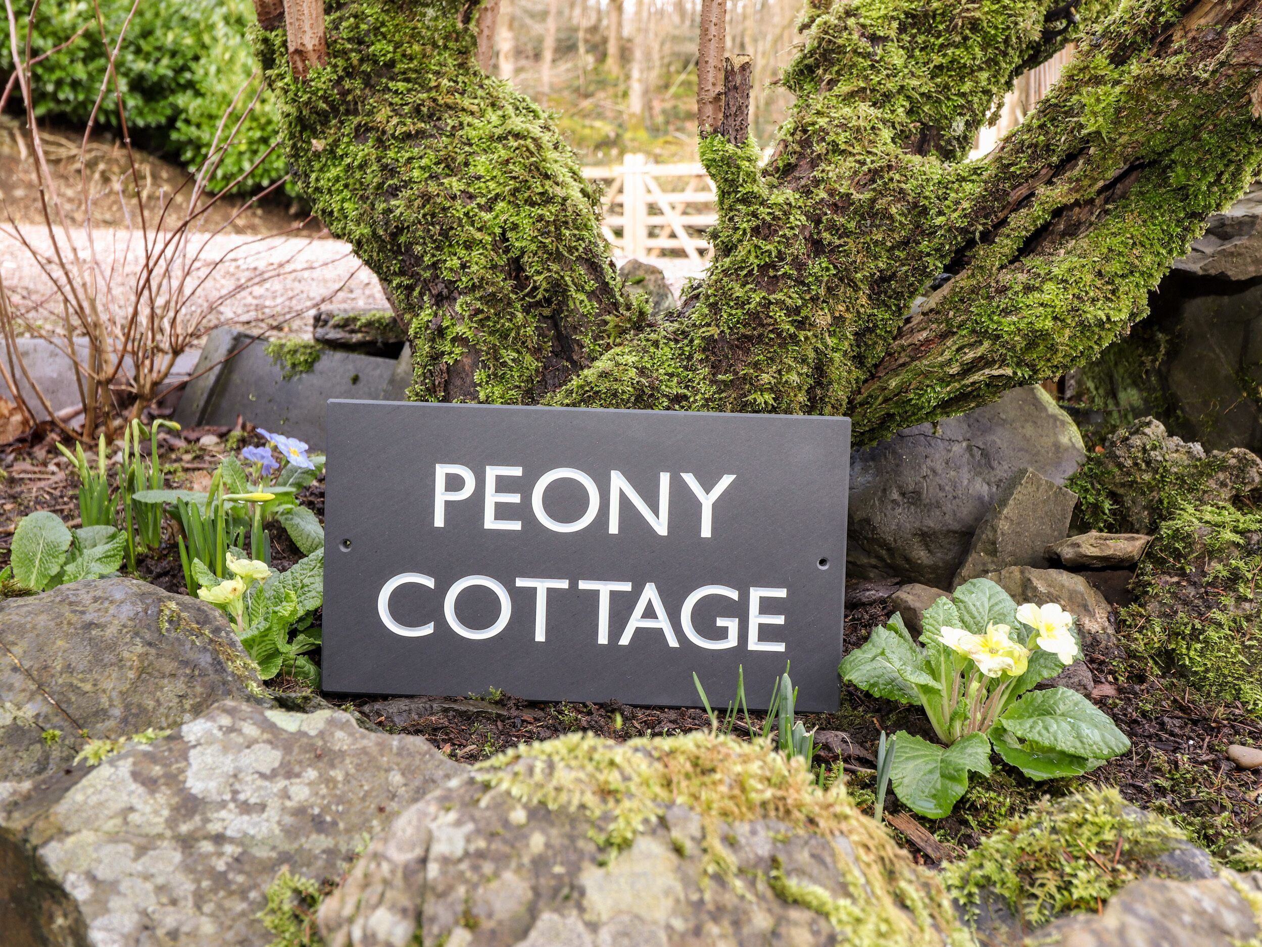 Placa com o nome 'PEONY COTTAGE' cercada por pedras e vegetação.
