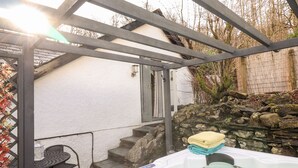 A hot tub under a pergola with a stone wall and steps leading to a door. - Peony Cottage (Ulverston)