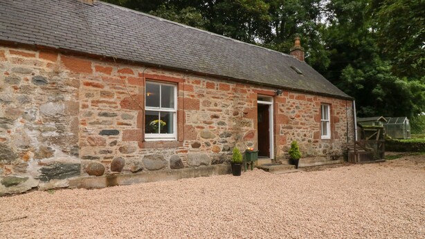 A stone house with a gravel driveway and a wooden fence. - Gardener's Cottage (Forfar)