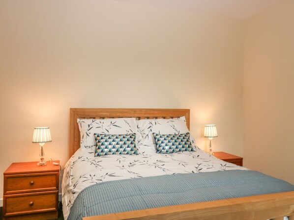 A neatly made bed with a patterned bedspread and pillows, flanked by two bedside tables with lamps. - Gardener's Cottage (Forfar)