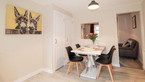 A dining area with a white table, black chairs, and a pendant light. There is a painting of donkeys on the wall and a door leading to another room. - Alturlie (Inverness)