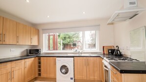 A modern kitchen with wooden cabinets, a built-in washing machine, a microwave, and a stove. - Alturlie (Inverness)