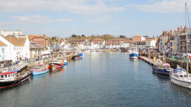 A harbor with boats docked along the piers, surrounded by buildings with various architectural styles. - Marina Reach (Weymouth)